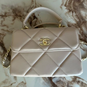  Chanel väska - Supersnygg beige handväska från Chanel i quiltat skinn med guldiga detaljer och kedjerem. Klassisk design med topphandtag och ikoniska CC-loggan framtill. Insidan är fodrad i vinrött och har flera fack!