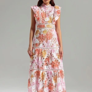 Ny klänning från Bella Barnett - Superfin långklänning med volangärmar och hög hals från Bella Barnett. Klänningen har ett broderat blommigt mönster i rosa, orange, vit och beige med spetsdetaljer och markerad midja. Perfekt för sommarens alla tillfällen!