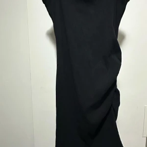 Svart ribbad klänning från SHEIN - Svart ribbad klänning från SHEIN med tight passform och snygg rynkdetalj på sidan. Klänningen är ärmlös och har en enkel, stilren look som passar perfekt när du vill känna dig extra snygg. Materialet är stretchigt och bekvämt. Det står L men passar från S till M.