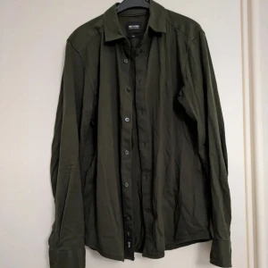 Mörkgrön skjorta från Only & Sons - Riktigt snygg mörkgrön skjorta från Only & Sons i mjuk 100% bomull, slim design. Klassisk krage, långa ärmar och knäppning framtill. Skjortan har en clean look utan mönster och passar perfekt till jeans eller chinos. Enkel och stilren design som funkar året runt. 