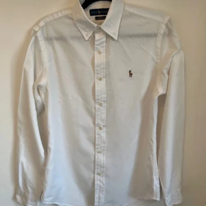 Vit skjorta från Ralph Lauren slim fit - Klassisk vit skjorta från Ralph Lauren i slim fit-modell. Skjortan har lång ärm, knappar framtill och ikoniska broderade loggan på bröstet. Nypris = 1700 kr mitt = 299 kr, skriv om minsta lilla fundering!