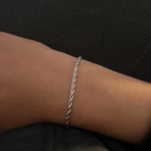 Tunt tvinnat silverarmband - Snyggt och stilrent armband i silverfärg med tvinnad design. Perfekt för dig som gillar minimalistiska smycken med lite edge. Lätt att matcha med andra accessoarer och har ett smidigt lås. Passar både tjejer och killar som vill ha något diskret men ändå unikt.