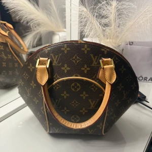  Monogram handväska L V - Säljer en ikonisk handväska  i klassiskt monogrammönster. Väskan är rundad med två stadiga handtag i ljust skinn och detaljer i guld. Materialet är canvas med skinn och väskan har snygga kontrastsömmar och exklusiv känsla.