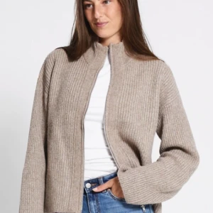 Beige ribbad cardigan jacka Lager 157 - Aldrig använd! Kostar 200 kr ny. Snygg beige cardigan jacka med ribbad struktur och hög krage. Jackan är stickad och har en avslappnad passform med långa ärmar. Perfekt att slänga på sig över en t-shirt för en chill och stilren look.