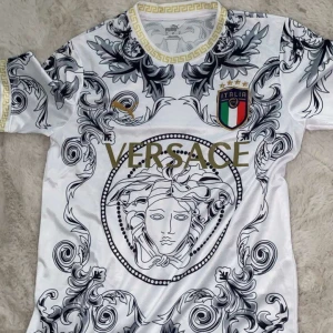 Italien x Versace x Puma fotbollströja - Unik vit fotbollströja i samarbete mellan Italien, Versace och Puma. Tröjan har korta ärmar, guldiga detaljer, stora Versace-loggan och Medusa-motiv framtill samt Italiens landslagsemblem. Snyggt svart och grått barockmönster över hela tröjan och guldfärgad kant vid hals och ärmslut. Den känns dock som att vara large.
