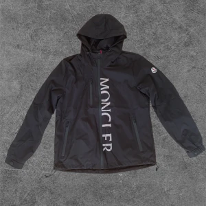 Moncler jacka - En Moncler jacka/windbreaker i storlek M men sitter som en S/XS. Den är helt ny aldrig använd. Vill du se hur jacka sitter kan du skriva privat så kan jag skicka bild och längd på modellen. Midjan och luvan går att justera med hjälp av spännen. 