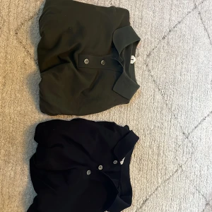 Två långärmade pikétröjor i svart och mörkgrön - Säljer två stilrena långärmade pikétröjor, en i svart och en i mörkgrön färg. Båda har klassisk krage och knäppning med tre knappar framtill. Perfekta för en clean och enkel look.