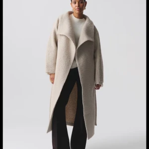 Beige lång kappa i bouclé från Gina Tricot - Säljer en beige lång kappa i bouclé från Gina Tricot. Kappan har en oversized passform, stora slag och är helfodrad. Perfekt för dig som vill ha en stilren och mysig look.