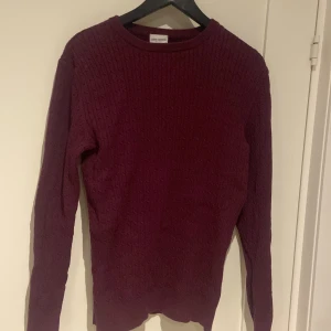 Vinröd stickad tröja från John Henric - Säljer en stilren vinröd stickad tröja från John Henric. Tröjan har ett klassiskt flätmönster och långa ärmar, perfekt för kyligare dagar. 