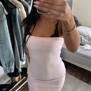 Ljusrosa ribbad långklänning - Säljer en ljusrosa ribbad långklänning med tight passform och axelbandslös design. Klänningen har en slits baktill och är perfekt för sommarens alla tillfällen. Enkel och stilren look som framhäver figuren.