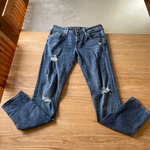 Jeans Jack & Jones - Säljer ett par blå skinny jeans från Jack & Jones, modell Liam. Jeansen har slitna detaljer på benen och klassisk femficksdesign. Perfekta för dig som gillar en tajt passform och trendiga slitningar. W31 L32. Knappt använda!