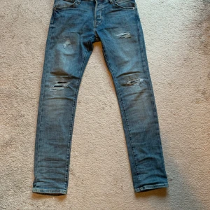 Jeans men slitningar - Säljer ett par ljusblå jeans med slitningar från jack&jones på både lår och knän. Klassisk femficksmodell med normal passform och raka ben. Perfekta för en avslappnad stil. Strl w30L32