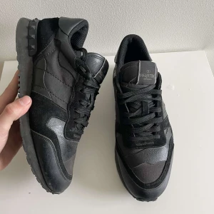 Svarta Valentino Rockrunner  - Säljer ett par svarta Valentino Rockrunner sneakers med coola nitar på hälen. Skorna har en mix av skinn och mocka, svarta skosnören och en platt sula. Perfekta för dig som gillar stilrena och exklusiva sneakers.