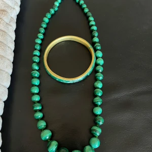 Malachite pärlhalsband och armband - Säljer ett snyggt set med ett malachite pärlhalsband och ett matchande armband. Halsbandet har runda pärlor i olika nyanser av grönt och armbandet är i guld med grön marmorering. Perfekt för att lyfta din outfit!