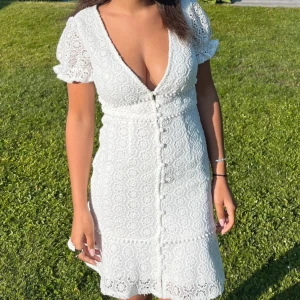 Vit spetsklänning med puffärm och knappar - Studentklänning! Superfin vit klänning med spets, v-ringning och puffärmar. Knappar framtill och figurnära passform. Jag är 160