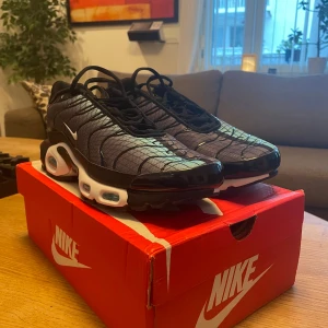 Nike Air Max Plus TN sneakers svart/blå - Nike Air Max Plus TN sneakers i svart och blått med vita detaljer. Skorna har ett vågigt mönster på ovandelen, synlig Air Max-dämpning och klassisk snörning. Snygg och sportig design med tydlig Nike-logga på sidan.