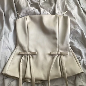 Beige korsettopp med rosetter Zara  - Snygg beige korsettopp med figurnära passform och två dekorativa rosetter framtill. Toppen har dragkedja i ryggen för enkel på- och avtagning. Perfekt för fest, den är från Zara I storlek M. Helt ny säljer då den är för liten på mig 