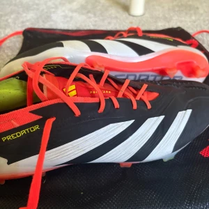 Adidas Predator fotbollsskor med röda detaljer - Säljer ett par Adidas Predator fotbollsskor i svart och vitt med röda snören och detaljer. Skorna har klassiska tre ränder på sidan och texten 'PREDATOR' på sulan. Perfekta för dig som vill sticka ut på planen. Väldigt bra använt nästan inget tecken på använt förutom lite på sulan nypris 3200 mitt pris 850 tveka inte på att höra av er vid fler frågor eller fler bilder köpare står för frakt😀😀