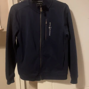 Marinblå tröja från Sail Racing - Snygg marinblå tröja från Sail Racing med dragkedja framtill och en bröstficka med logga. Tröjan har lång ärm och en sportig look, perfekt för dig som gillar stilrena plagg. Skriv för fler funderingar eller frågor💯💯