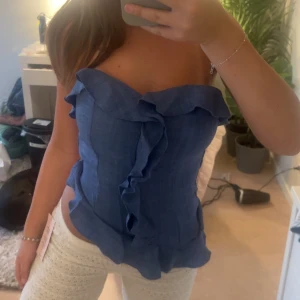 Blå volangig tubtopp - Säljer en blå tubtopp med volangdetaljer framtill och längs överkanten. Toppen har en feminin och trendig look, perfekt för varma dagar.