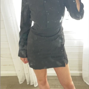 Svart skjortklänning från MNG - Stilren svart skjortklänning från MNG med långa ärmar och knappar framtill. Klänningen har en figurnära passform och kort längd, perfekt för en trendig look. Enkel design som passar till många tillfällen.