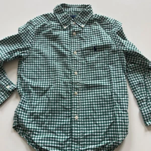  skjorta från Ralph Lauren - Klassisk grön och vit rutig skjorta från Ralph Lauren med broderad logga på bröstet. Skjortan har knappar hela vägen och lång ärm, perfekt för en stilren look. För barn 