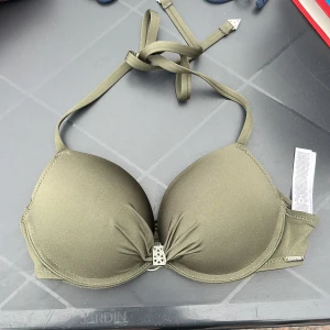 Oanvänd grön bikinitopp - Säljer en helt oanvänd bikinitopp från New Yorker i storlek 70B. Superfin militärgrön färg med smycke i mitten. Säljer för 20kr plus frakt, välj gärna instabox om möjligt
