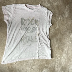 Vit t-shirt med Rock & Roll-tryck från Zadig & Voltaire - Vit t-shirt från Zadig & Voltaire med blekt 'Rock & Roll'-tryck framtill. Rund halsringning och korta ärmar. 