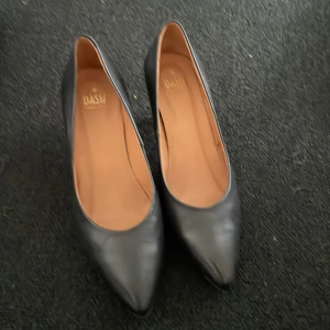 Svarta pumps med klack från Dasu - Klassiska svarta pumps med spetsig tå och smal klack från Dasu. Skorna har en elegant och tidlös design i slätt material och passar perfekt till många olika outfits.