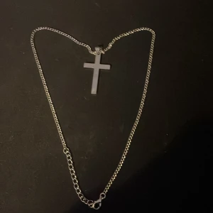 Silverfärgat halsband med kors - Snyggt halsband i silverfärg med ett stilrent kors som hänge. Kedjan är tunn och klassisk, perfekt för att ge en enkel men cool touch till din outfit.
