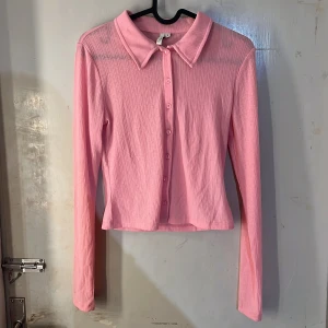 Topp - Säljer en ljusrosa, transparent skjort topp  från NLY Trend i storlek S. Skjortan har långa ärmar, klassisk krage och knäppning framtill. Materialet är lätt och något ribbat, perfekt för lager-på-lager eller som statement-plagg.