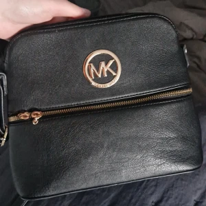 Svart axelväska från Michael Kors - Säljer min använda svarta axelväska från Michael Kors. Väskan har en del trasiga dragkedjor på flera ställen, men går att använda ändå! OBS! Inte äkta! Priset går att diskutera.