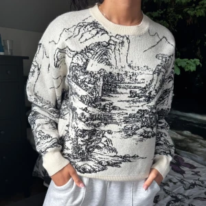 Beige stickad tröja med svart landskapsmönster - Säljer en beige stickad tröja med svart konstnärligt landskapsmönster. Tröjan har rund halsringning och långa ärmar med ribbade muddar. Köpt från Cider i storlek S.