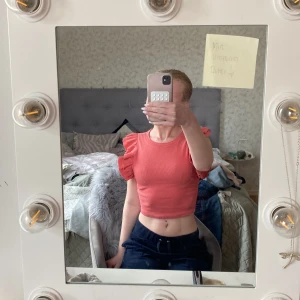 Aprikos färgad croppad topp med volangärmar från Zara - Säljer en söt croppad topp från Zara i en härlig aprikos färg. Toppen har volangdetaljer på axlarna och är ribbad i materialet. Perfekt för sommaren och ger en trendig look.