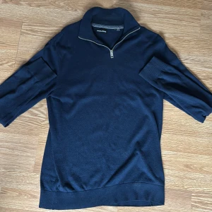 Mörkblå stickad tröja med dragkedja från Jack & Jones - Mörkblå stickad tröja från Jack & Jones med halv dragkedja vid kragen. Tröjan har långa ärmar och ribbade muddar vid ärmslut och nederkant. Perfekt för lager-på-lager och stilren look.