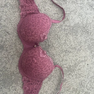 Lila spets-bh från Hunkemöller - Säljer en snygg lila bh från Hunkemöller med blommig spets. Detta är en vanlig t-shirts bh, ingen pushup. Bh:n har en liten rosett och dekorativ detalj framtill. Perfekt för dig som vill ha något både bekvämt och stilrent. Den är nog bara använd max 5 gånger. Hör av er vid fler bilder eller frågor!💛
