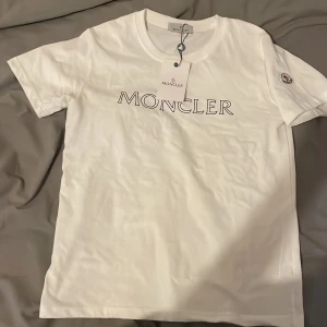 Vit moncler t-shirt - Säljer en klassisk vit tshirt från Moncler med tryckt logga på bröstet och broderad Moncler-patch på ärmen. T-shirten har rund hals och korta ärmar. Perfekt för en stilren och enkel look. Kom dm för mer info✌️💵