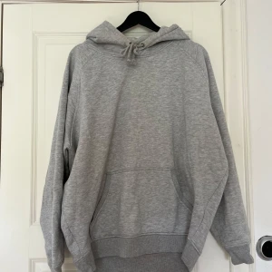 Grå hoodie - En klassisk grå hoodie med huva och dragsko samt stor magficka framtill. Perfekt för en avslappnad stil och enkel att matcha med det mesta. Mjuk och bekväm med långa ärmar. Snygg passform.
