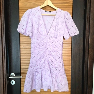 Ljuslila kortklänning med puffärm och v-ringning med broderie anglaise - Superfin ljuslila klänning från Zara med v-ringning, puffiga kortärmar och rynkade detaljer framtill. Klänningen har ett blommigt mönster och volang nertill. Perfekt för sommarens tillfällen! Använd en gång. 