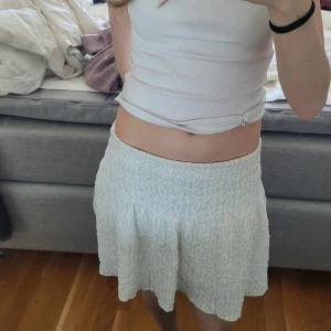 Vit kortkjol med struktur - Säljer en söt vit kortkjol med strukturmönster. Kjolen har en lätt utsvängd form och resår i midjan för en bekväm passform. Perfekt för varma dagar och enkel att matcha med olika toppar.