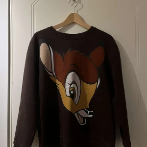 Brun sweatshirt med Bambi-tryck - Säljer en brun sweatshirt med stort Bambi-tryck framtill. Tröjan har rund halsringning och långa ärmar. Perfekt för dig som gillar Disney och vill ha en mysig och snygg tröja.
