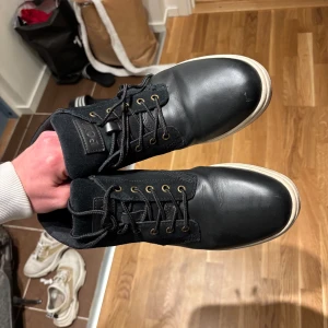 Svarta sneakers från Polo Ralph Lauren - Svarta sneakers från Polo Ralph Lauren med vit sula och bruna detaljer undertill. Skorna har snörning med metallhål och är tillverkade i en kombination av skinn och syntet. Klassisk Polo-logga på sidan och märkesdetalj på tungan.