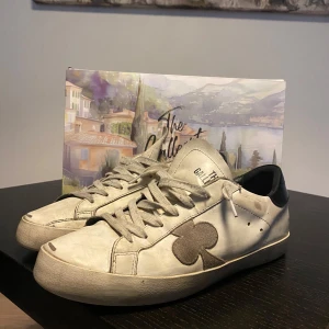 Vita sneakers från The Gallerist med svart klöver - Säljer ett par the gallerist som ändå är i hyfsat skick dem har börjat släppa lite i kanten och lite slitna under sulan. Men annars är dem i bra skick. Priset ej hugget i sten.