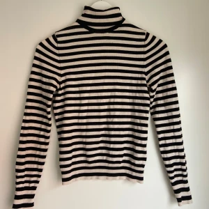 Svartvit randig polotröja - Säljer en svartvit randig polotröja med långa ärmar. Tröjan är figurnära och har klassisk polokrage, perfekt för lager-på-lager eller som statement-piece.