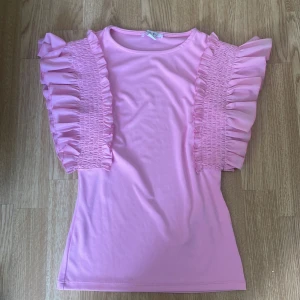 Rosa topp med volangärmar - Säljer en rosa topp från Amisu med unika volangärmar och smockdetaljer längs axlarna. Toppen har rund halsringning och är tillverkad i ett mjukt, stretchigt material. Pris kan som vanligt diskuteras 💕 Har bara testat ungefär 1 gång så nästan helt ny med inga tecken på and vändninginnan!