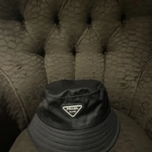 Svart bucket hat från Prada - Pris är spikat :) Snygg svart bucket hat från Prada med klassisk trekantig logotyp framtill. Hatten har en enkel och stilren design i slätt material, perfekt för att lyfta vilken outfit som helst.