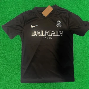 Svart PSG x Balmain fotbollströja - Snygg svart fotbollströja från Nike i samarbete med PSG och Balmain. Tröjan har korta ärmar, rund hals och tryck med Balmain Paris-logga samt PSG-emblem på bröstet. Perfekt för dig som gillar stilrena och exklusiva matchtröjor.