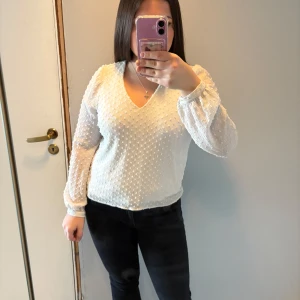 Vit blus med v-ringning - Säljer en elegant vit blus med v-ringning och långa ärmar. Blusen har ett diskret prickigt mönster och knappar vid ärmsluten. Perfekt för en stilren look.