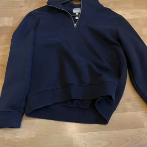 Mörkblå tröja med dragkedja från H&M - Säljer en stilren mörkblå tröja från H&M med dragkedja vid halsen. Tröjan har långa ärmar och ribbade muddar vid ärmslut och nederkant. Perfekt för en avslappnad look.