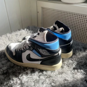 Nike Air Jordans i svart, vitt och blått - Säljer ett par Nike Air Jordans i en snygg kombination av svart, vitt och blått. Skorna har den klassiska snörningen och en ikonisk design som passar perfekt för sneakerälskare. 36-37 köpta för 2899, skolåda och creasingskydd medföljer